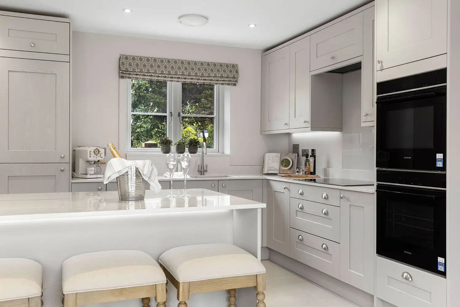Kitchen with panelled cupboard doors in a light grey, beige colour with island and light stools